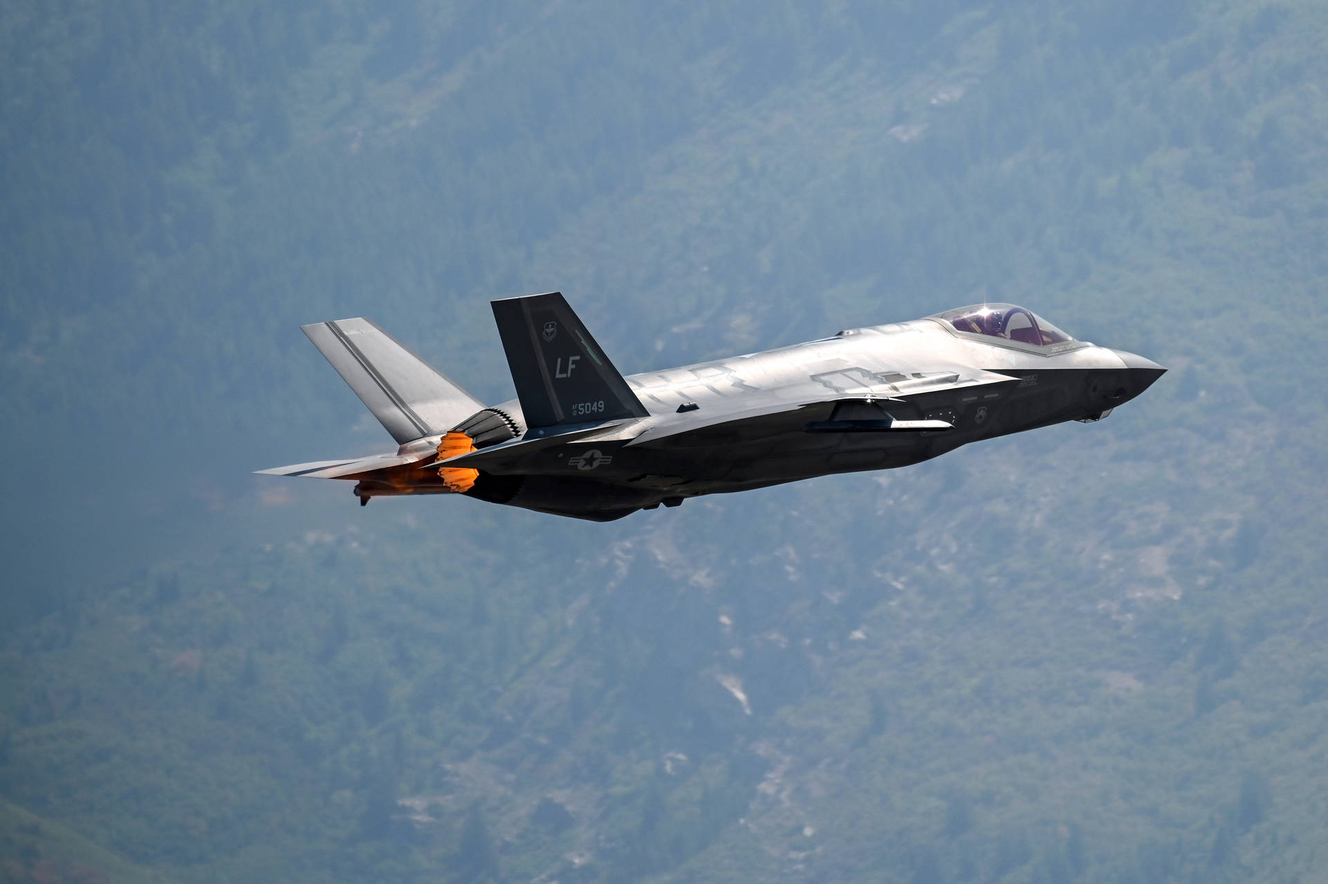 a f-15 fighter jet flying over a mountain Wallpaper