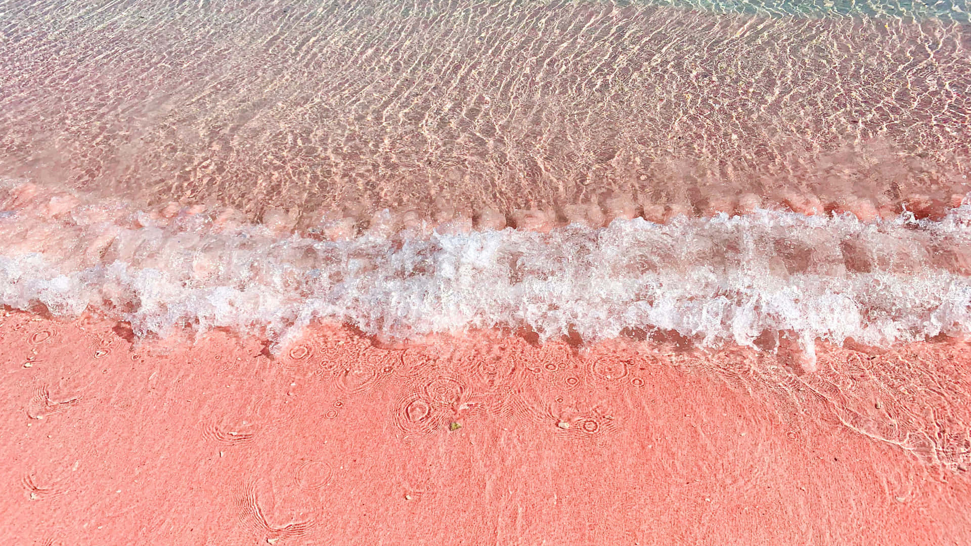 A Pink Beach With Waves And Sand