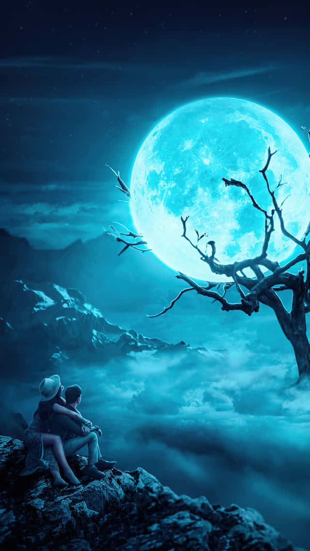 A Couple Sitting On A Rock Looking At The Moon Wallpaper