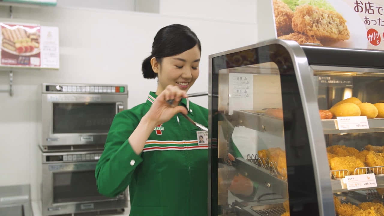 A Woman In Green Is Putting Food Into A Display Case