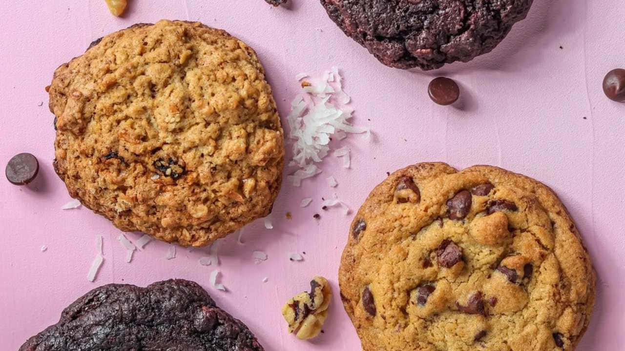 Four Cookies With Chocolate Chips And Nuts On A Pink Background