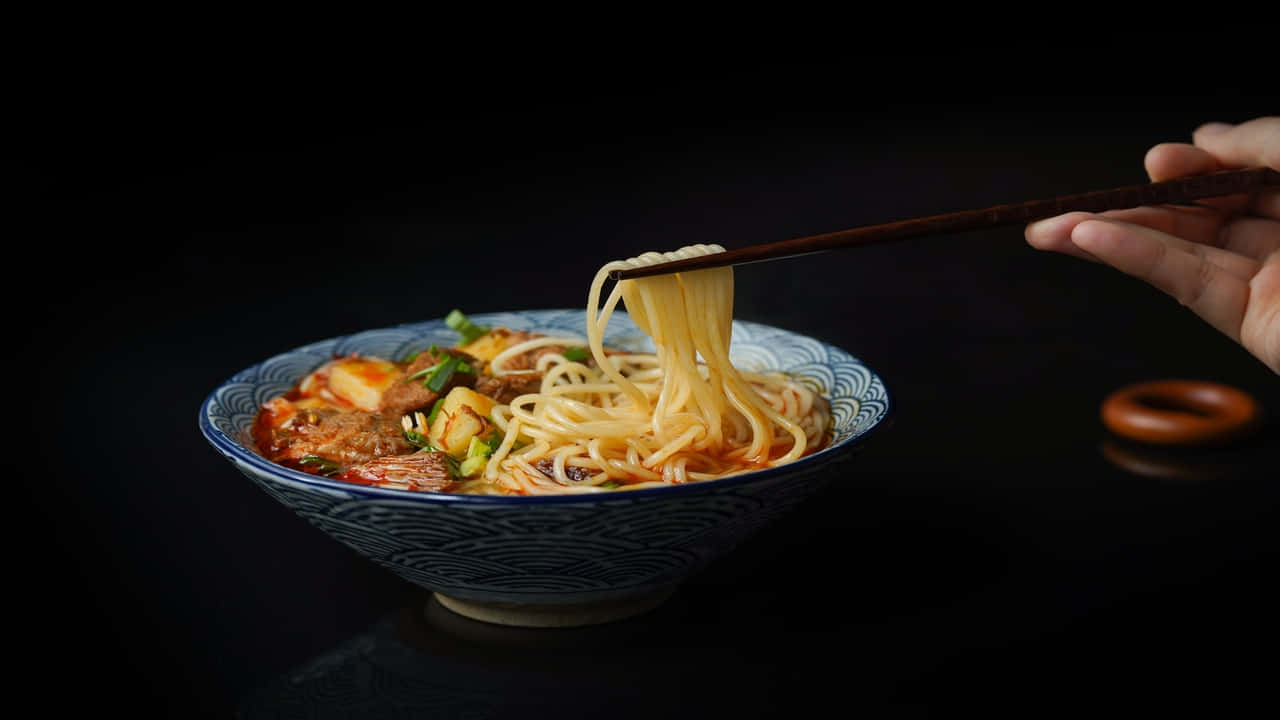 A Person Is Holding A Bowl Of Noodles With Chopsticks