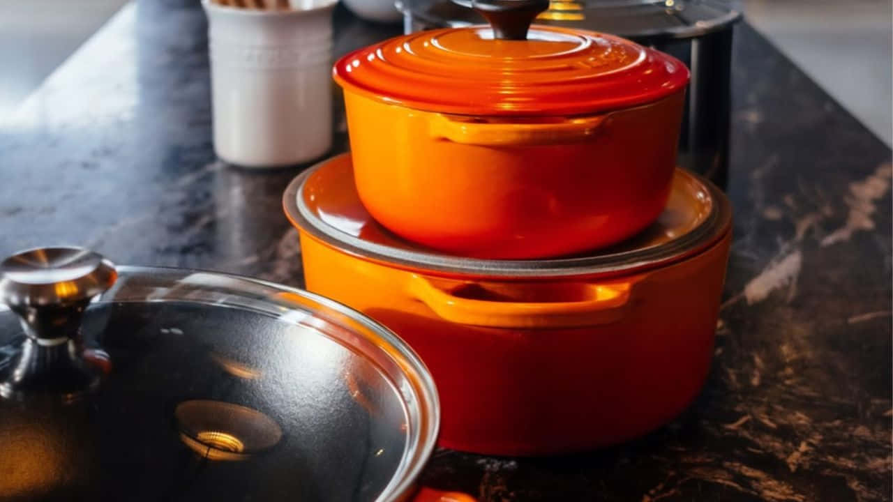 A Set Of Orange Pots And Pans On A Counter