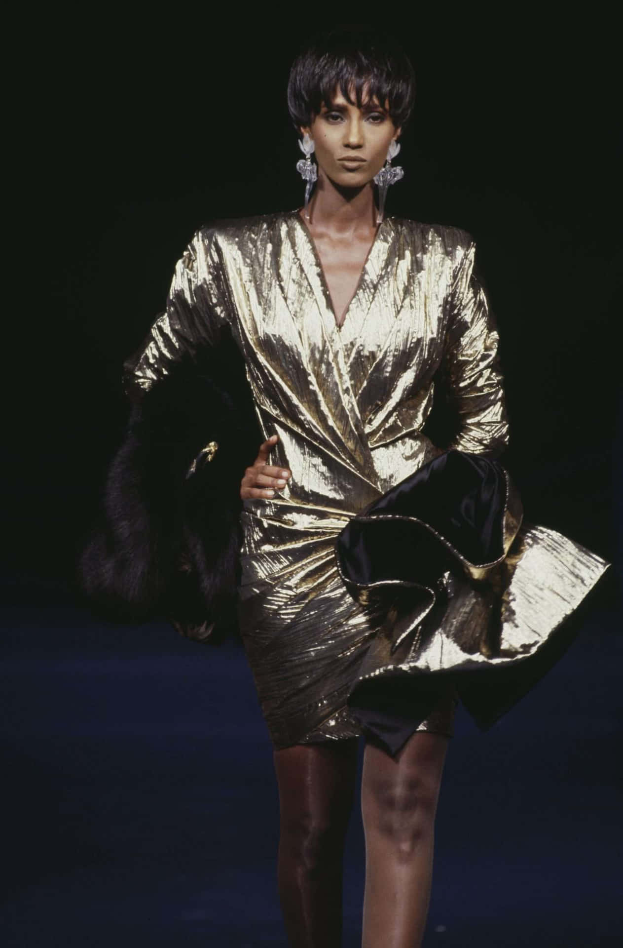 A Woman In A Gold Dress Walking Down The Runway
