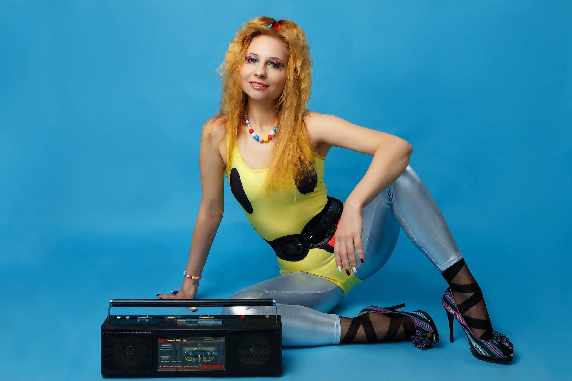A Woman In A Metallic Outfit Sitting On A Blue Background With A Boombox