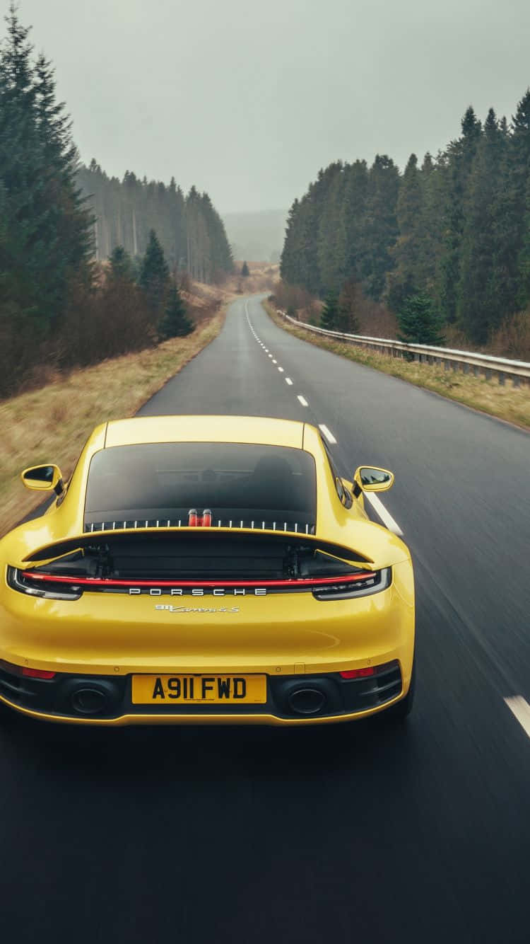 Bagenden af en gul Porsche Cayman kører ned ad en vej. Wallpaper