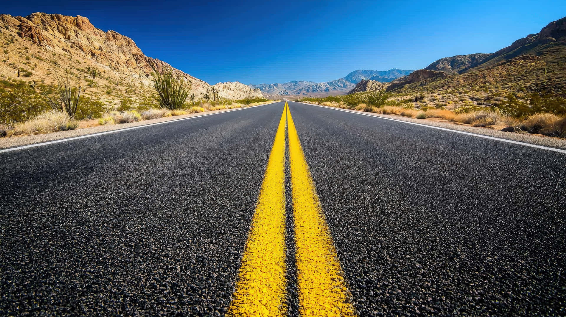 A Long, Open Desert Highway Stretches Into The Horizon, Surrounded By Arid Mountains Wallpaper