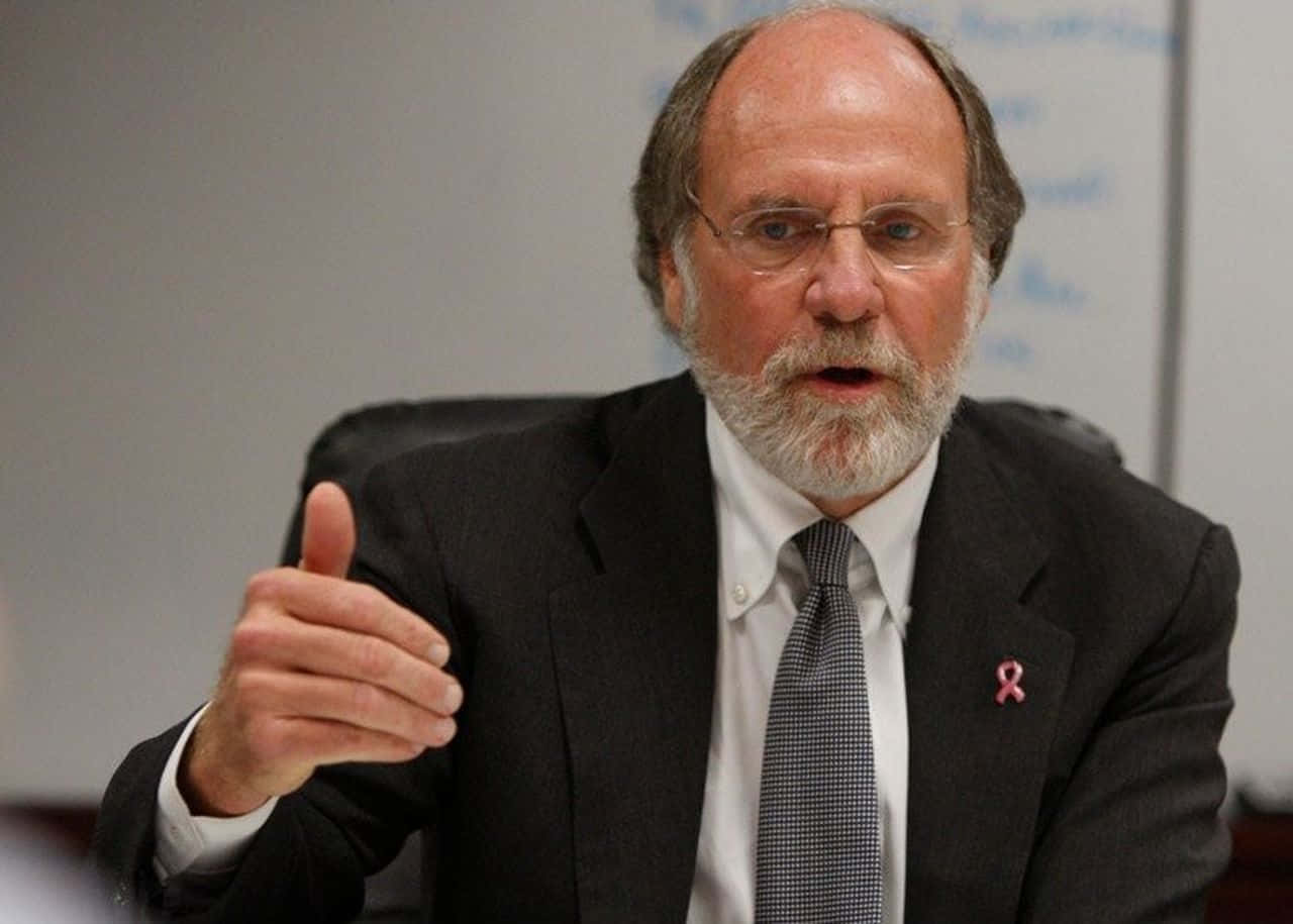 A Thoughtful Jon Corzine Leaning On His Desk Wallpaper