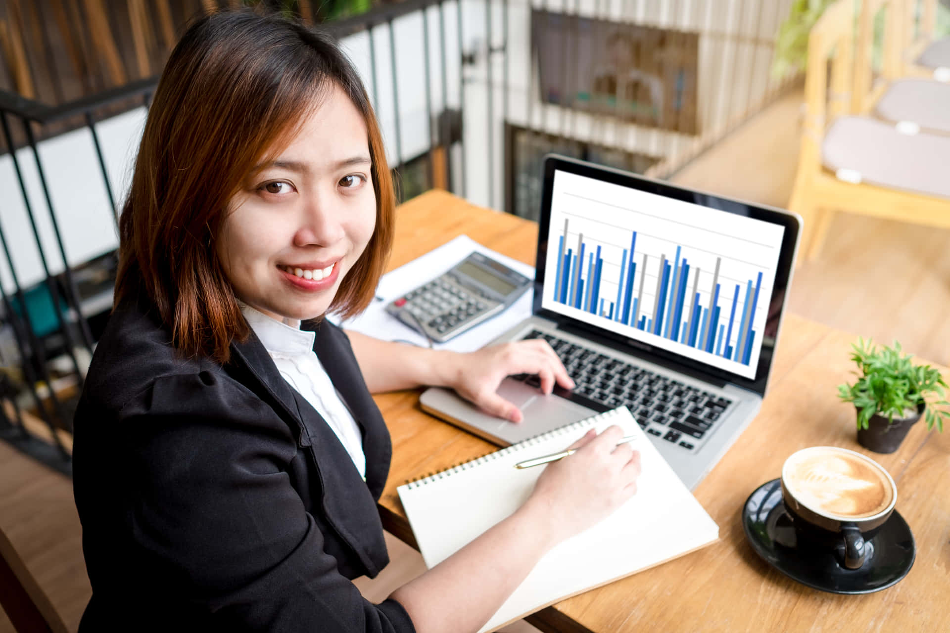 Asian Woman Sitting At A Desk With A Laptop And Graphs