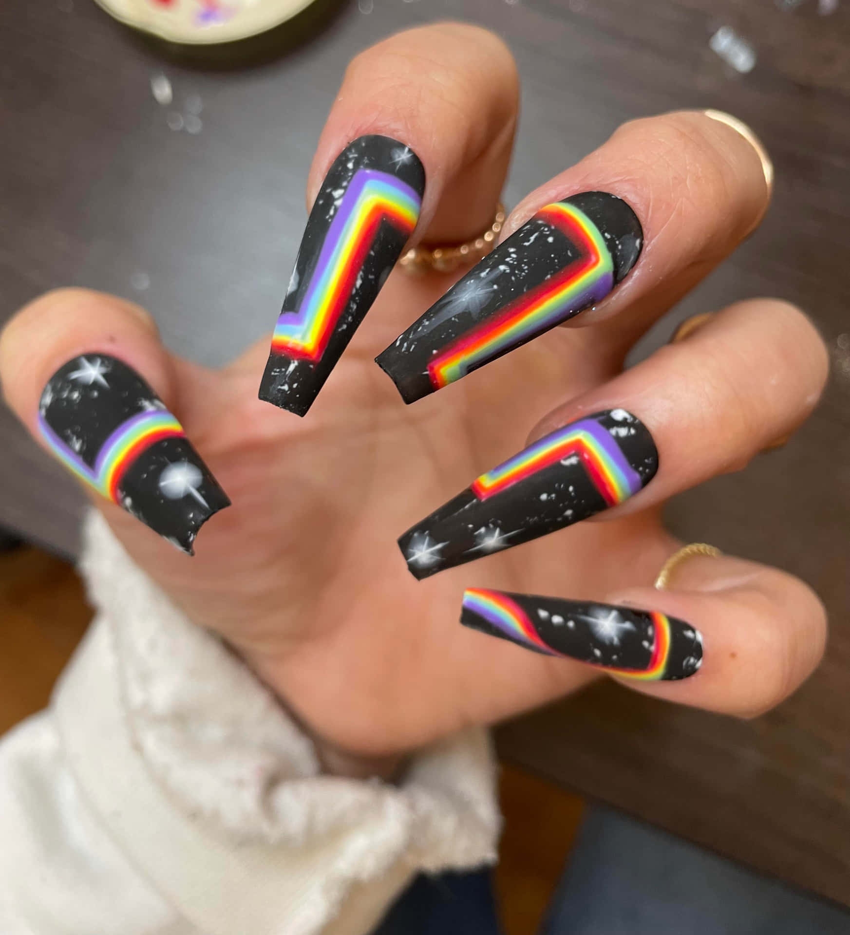 A Woman Holding Up A Black Nail With Rainbow Designs Wallpaper
