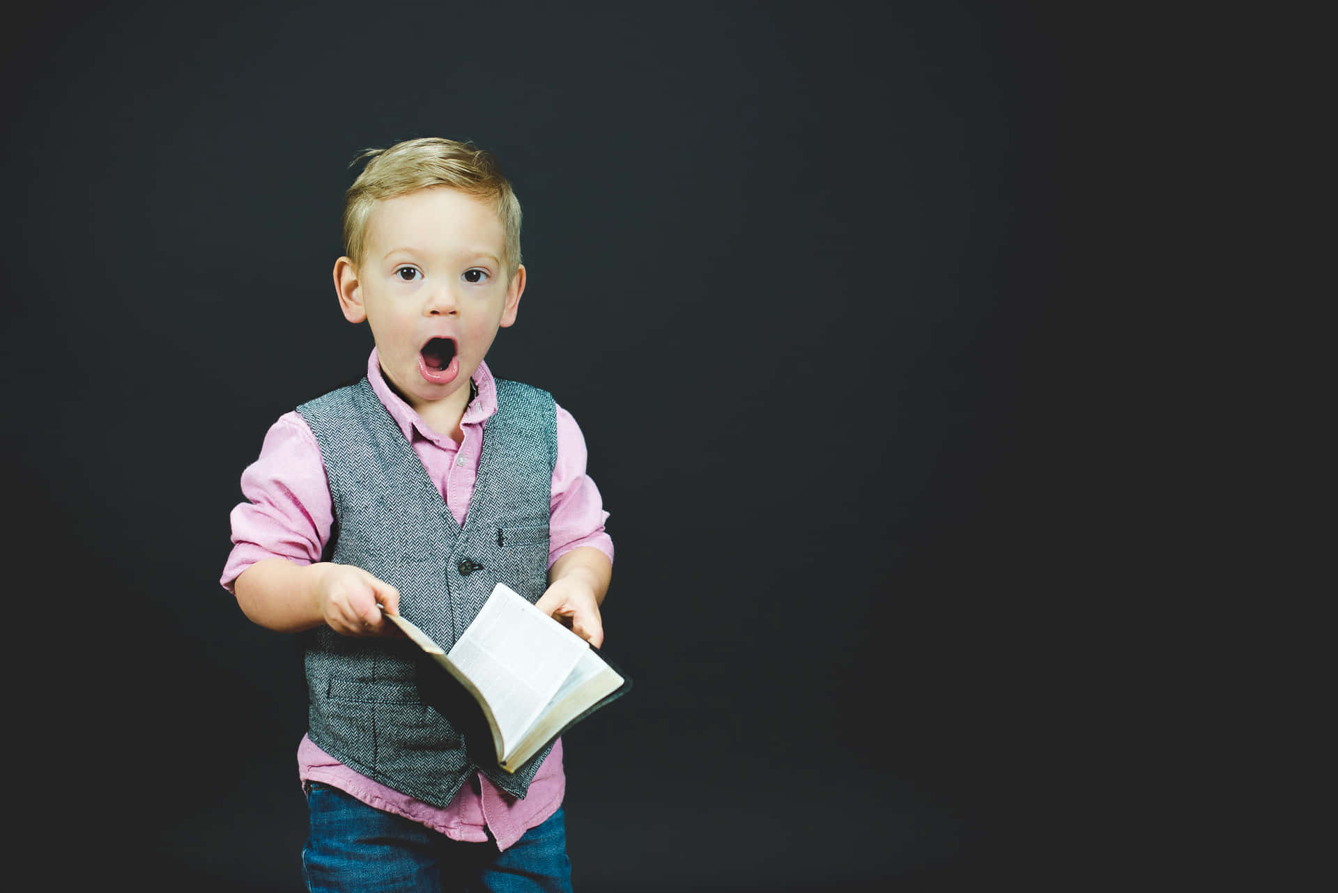 A Young Boy Holding A Book And Looking Surprised Wallpaper