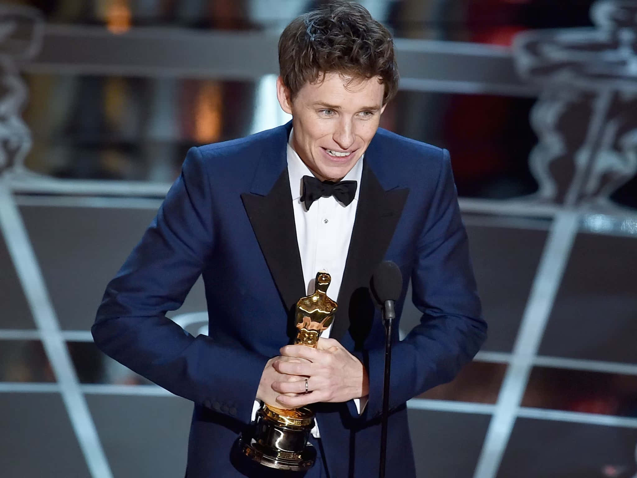 A Man In A Tuxedo Holding An Oscar Award