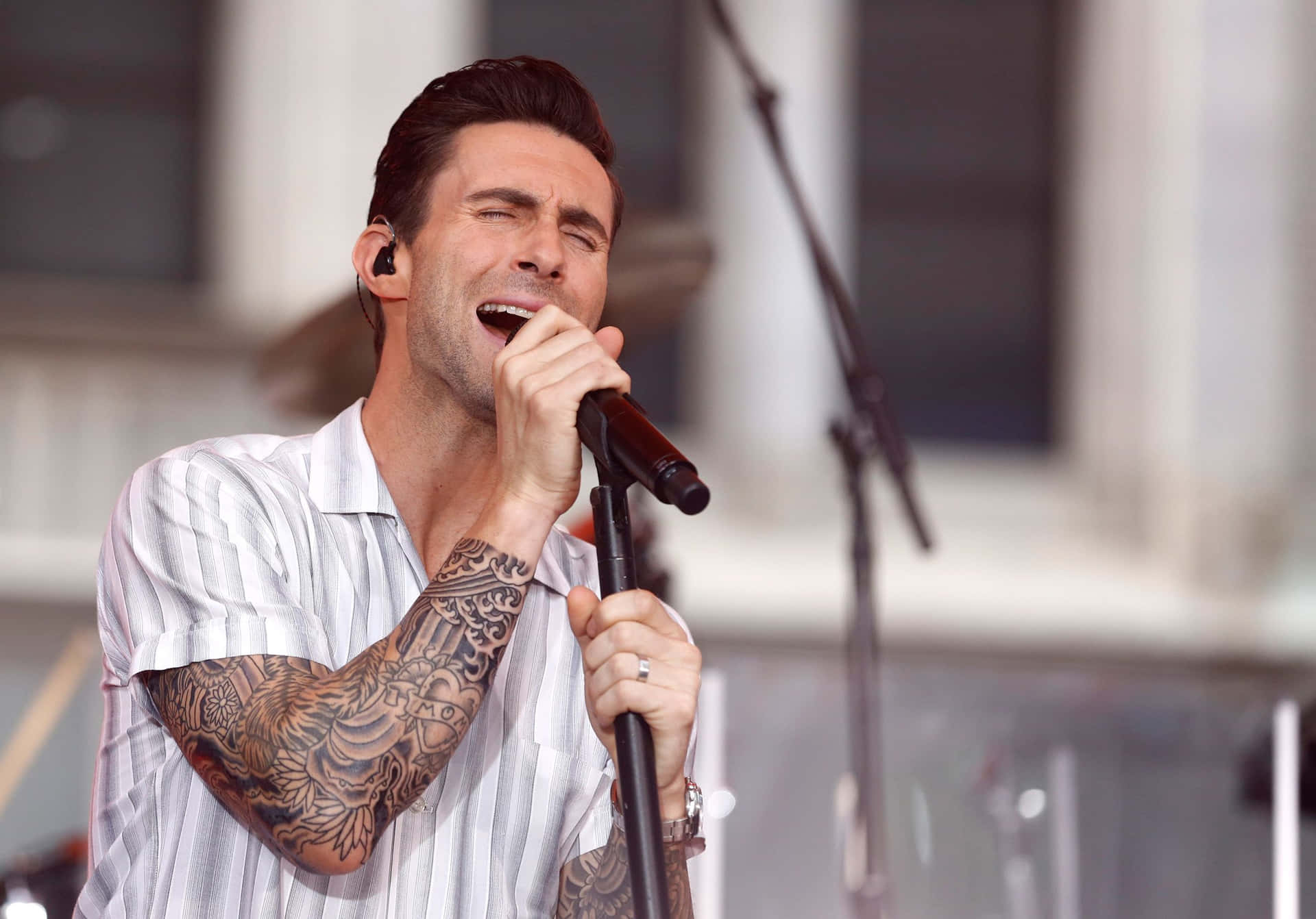 A Man With Tattoos Singing Into A Microphone