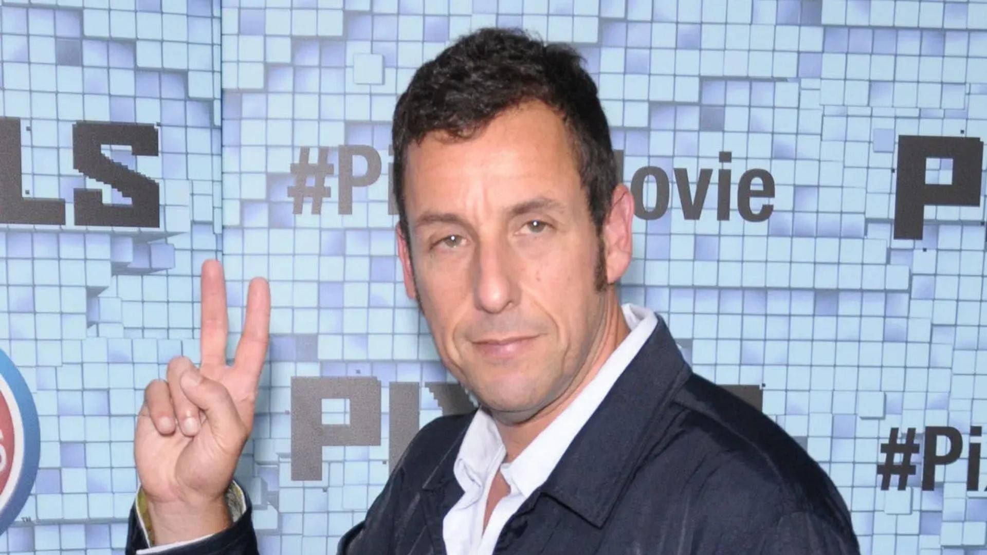 Caption: Adam Sandler flashing a peace sign with a charming smile. Wallpaper