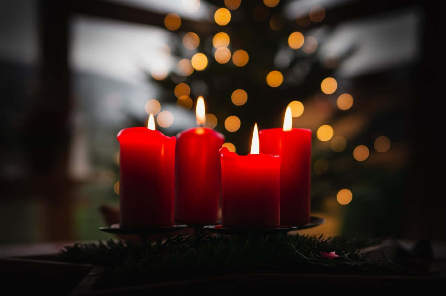 Three Red Candles Are Lit In Front Of A Christmas Tree
