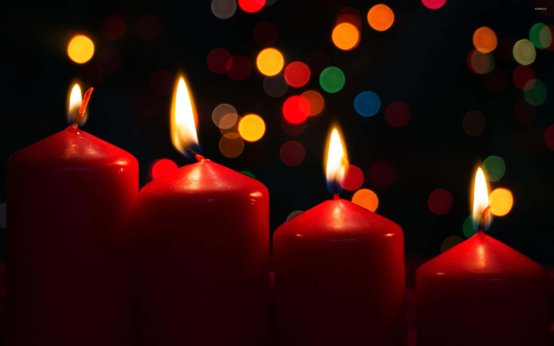 Three Red Candles Lit In Front Of A Colorful Background