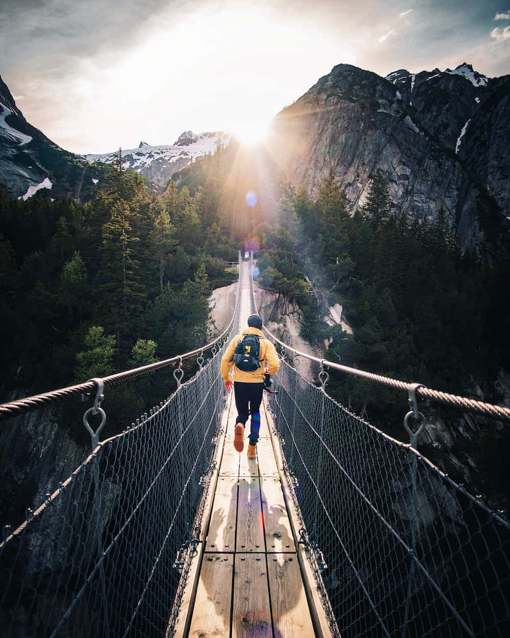 A Man Walking Across A Suspension Bridge In The Mountains
