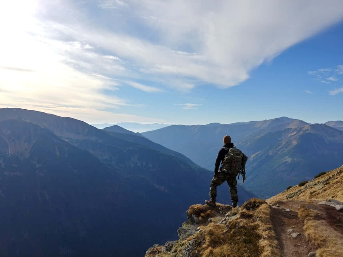 A Man Is Standing On A Mountain Top Looking At The Mountains