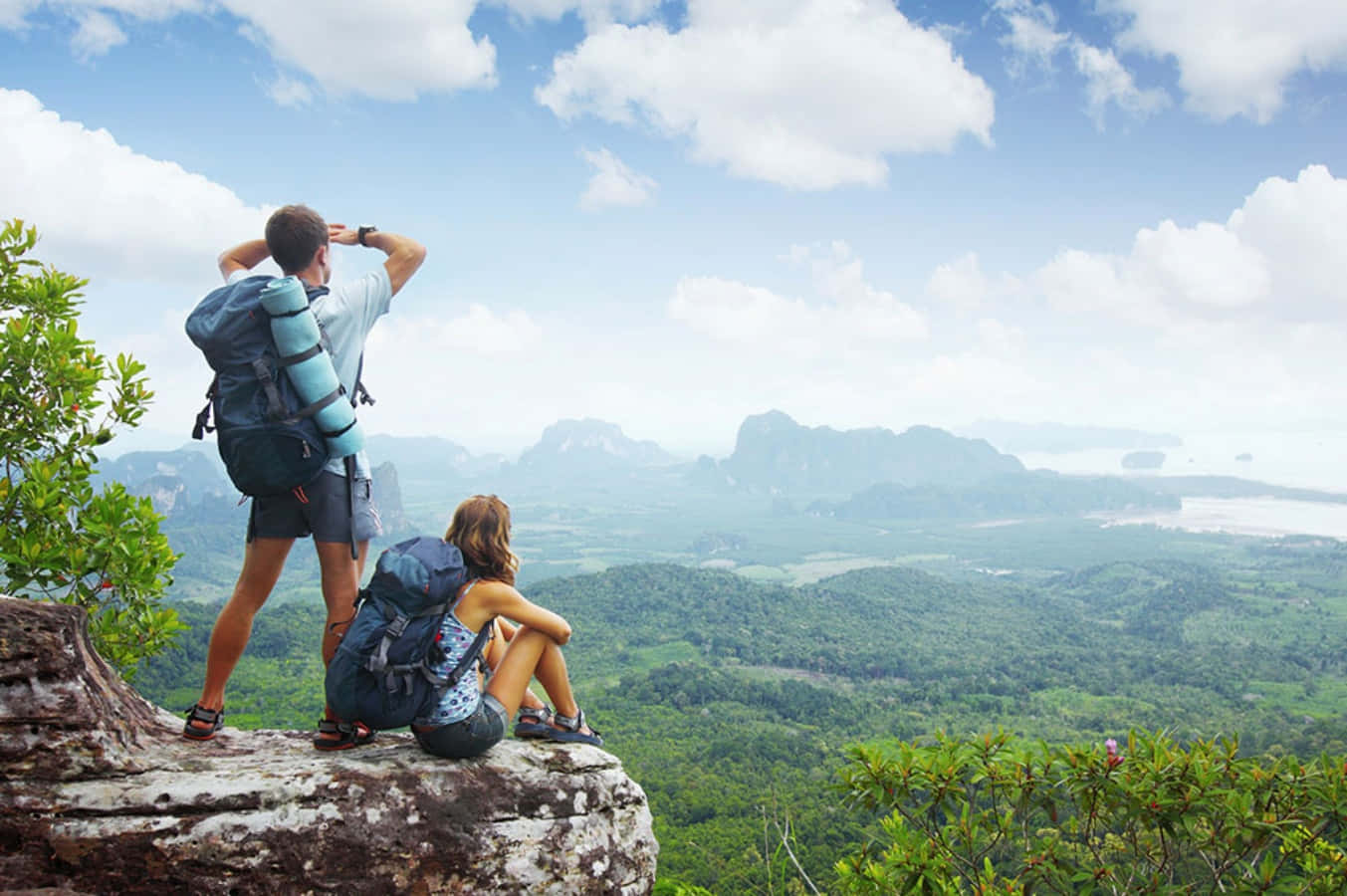 Two People With Backpacks Standing On A Cliff Overlooking A Mountain