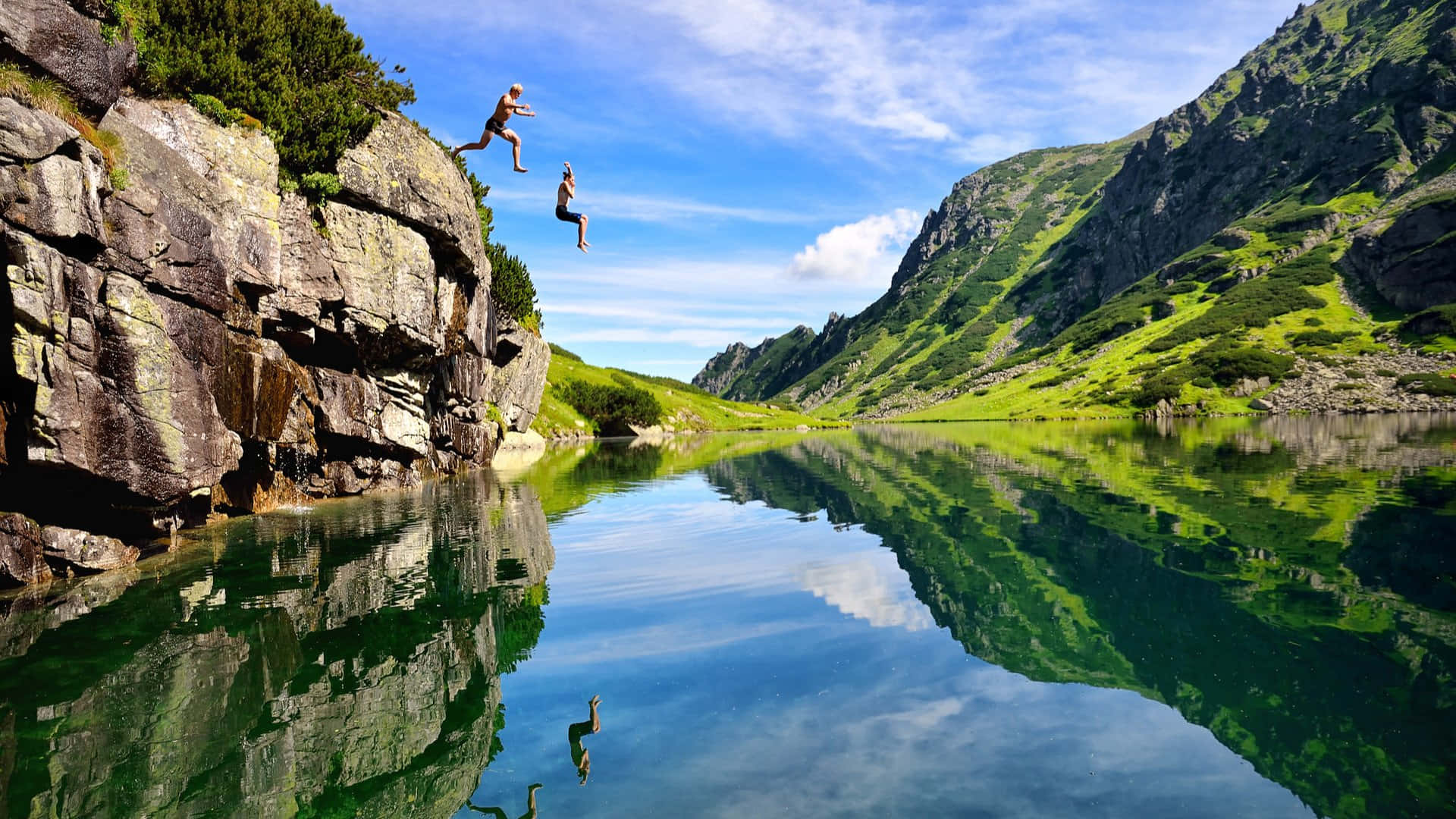 Two People Jumping Off A Cliff Into A Lake