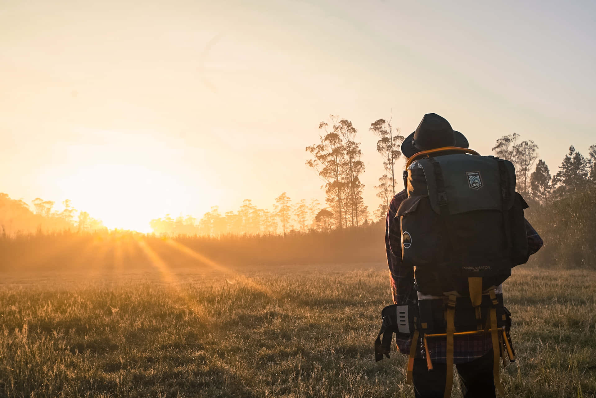 Eineperson Mit Einem Rucksack Steht In Einem Feld Bei Sonnenuntergang.