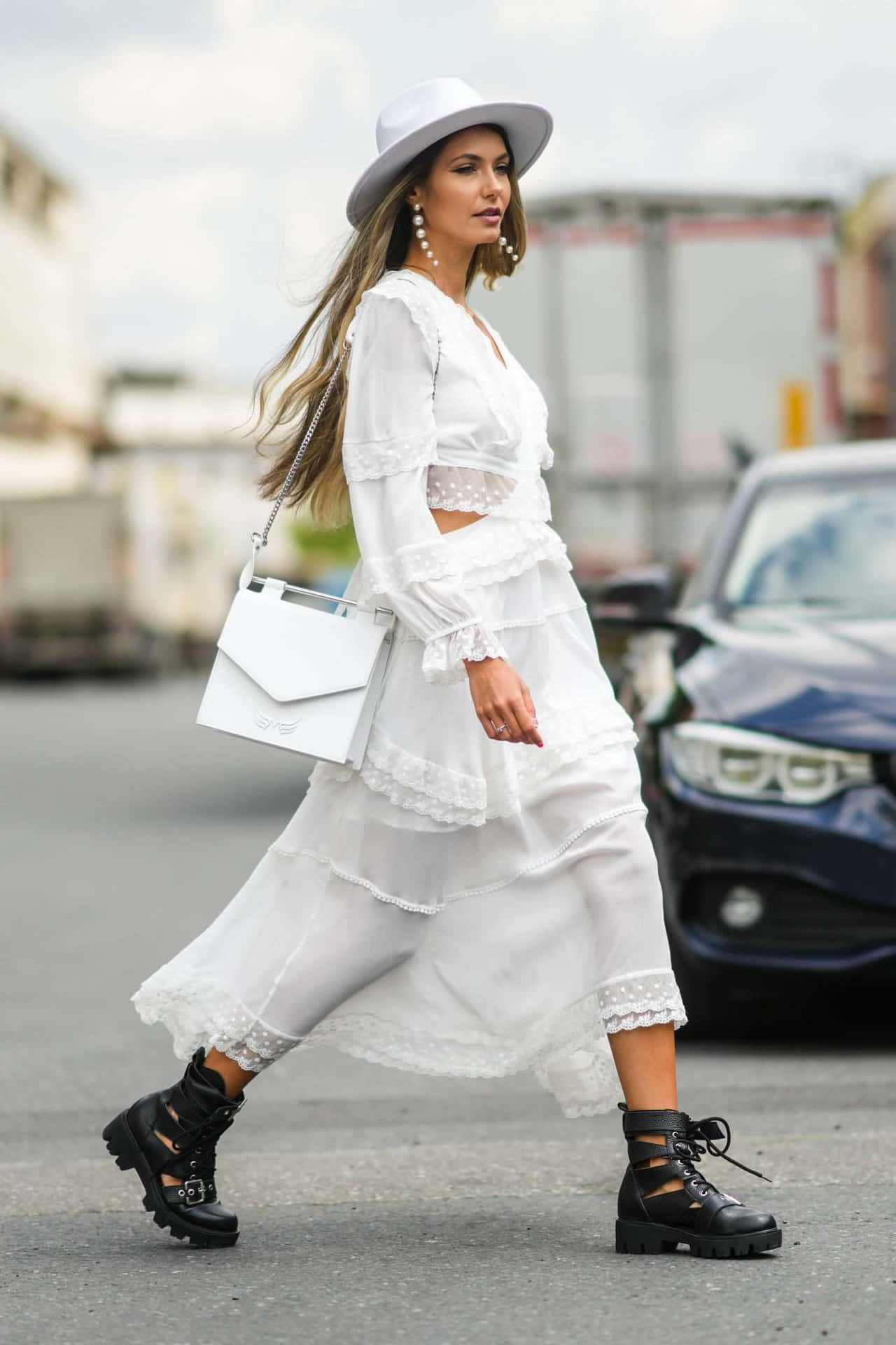 A Woman In A White Dress And Hat Walking Down The Street