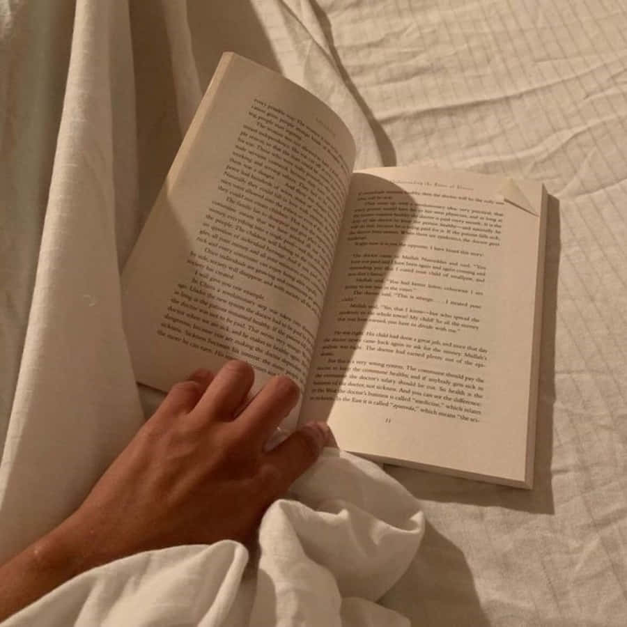 A Person Reading A Book On A Bed