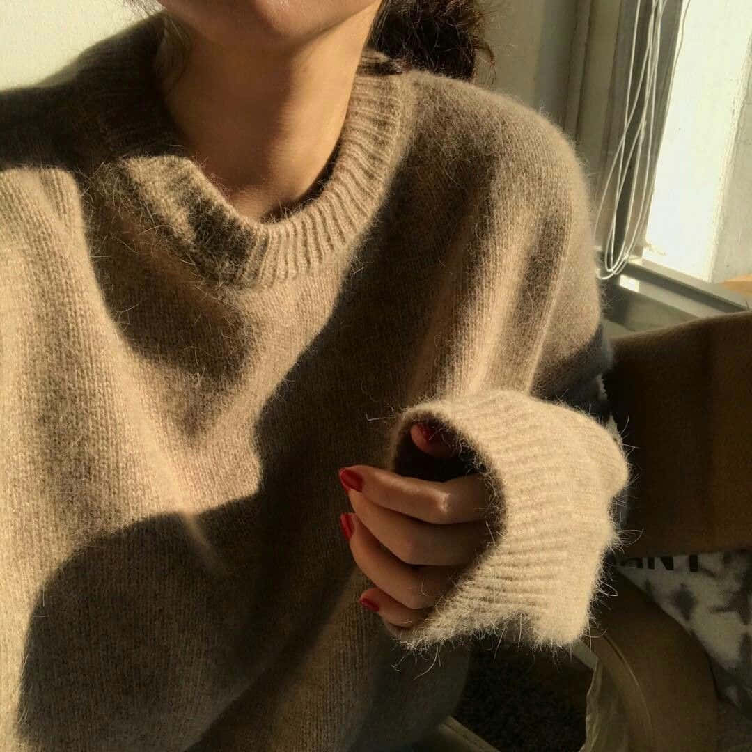 A Woman Wearing A Beige Sweater With Red Nails