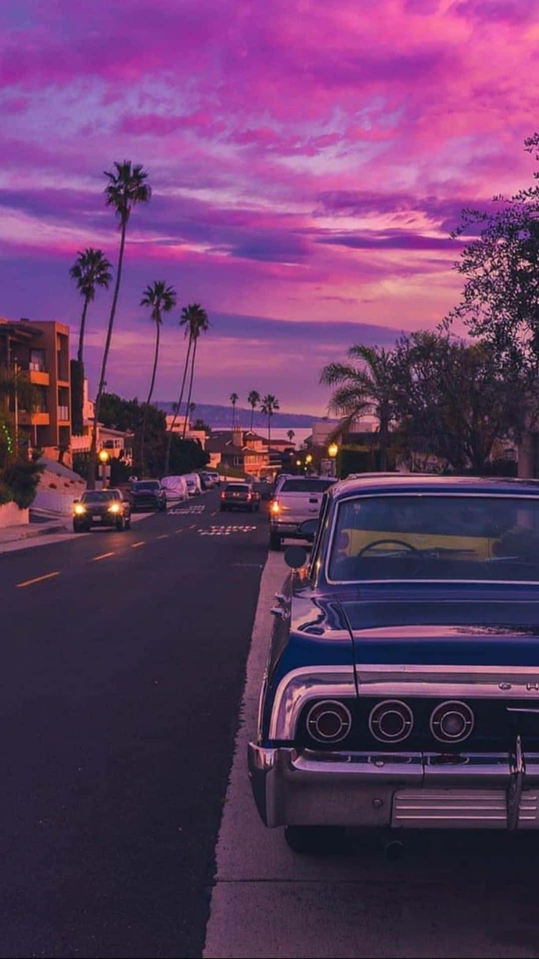 A Classic Car Parked On The Street At Sunset Wallpaper