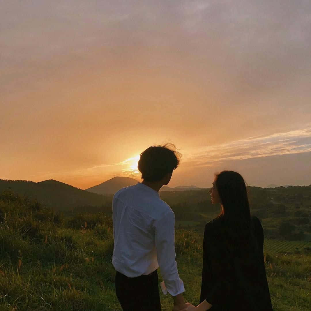 A Couple Holding Hands In A Field At Sunset