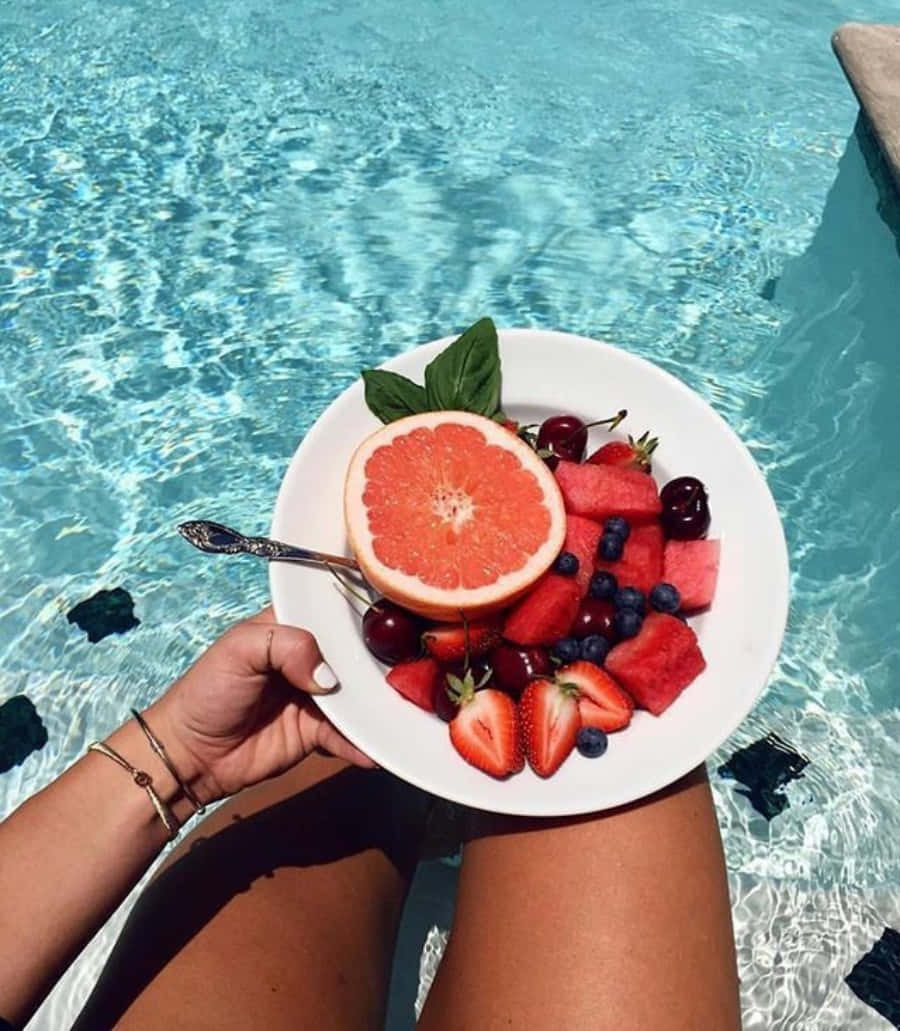 A Woman Holding A Plate Of Fruit By A Pool