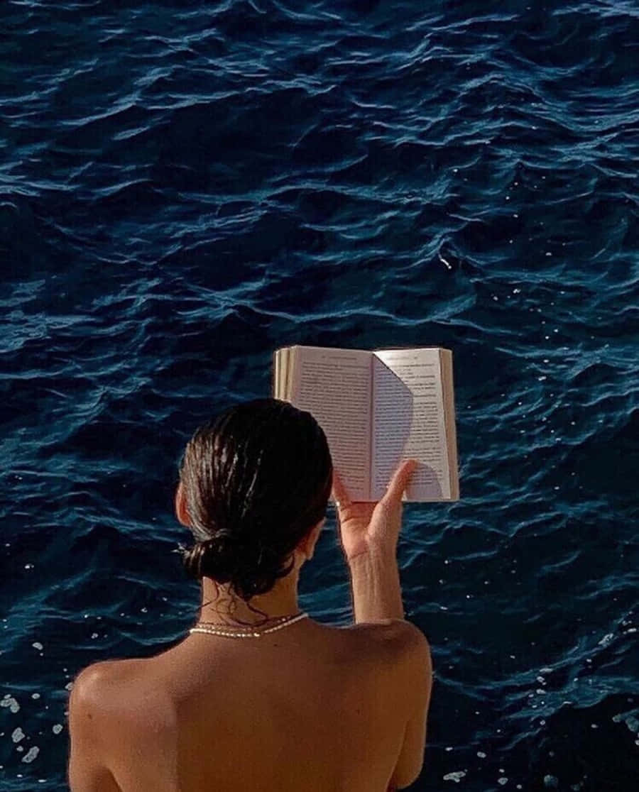 A Woman Reading A Book On A Boat In The Ocean Wallpaper