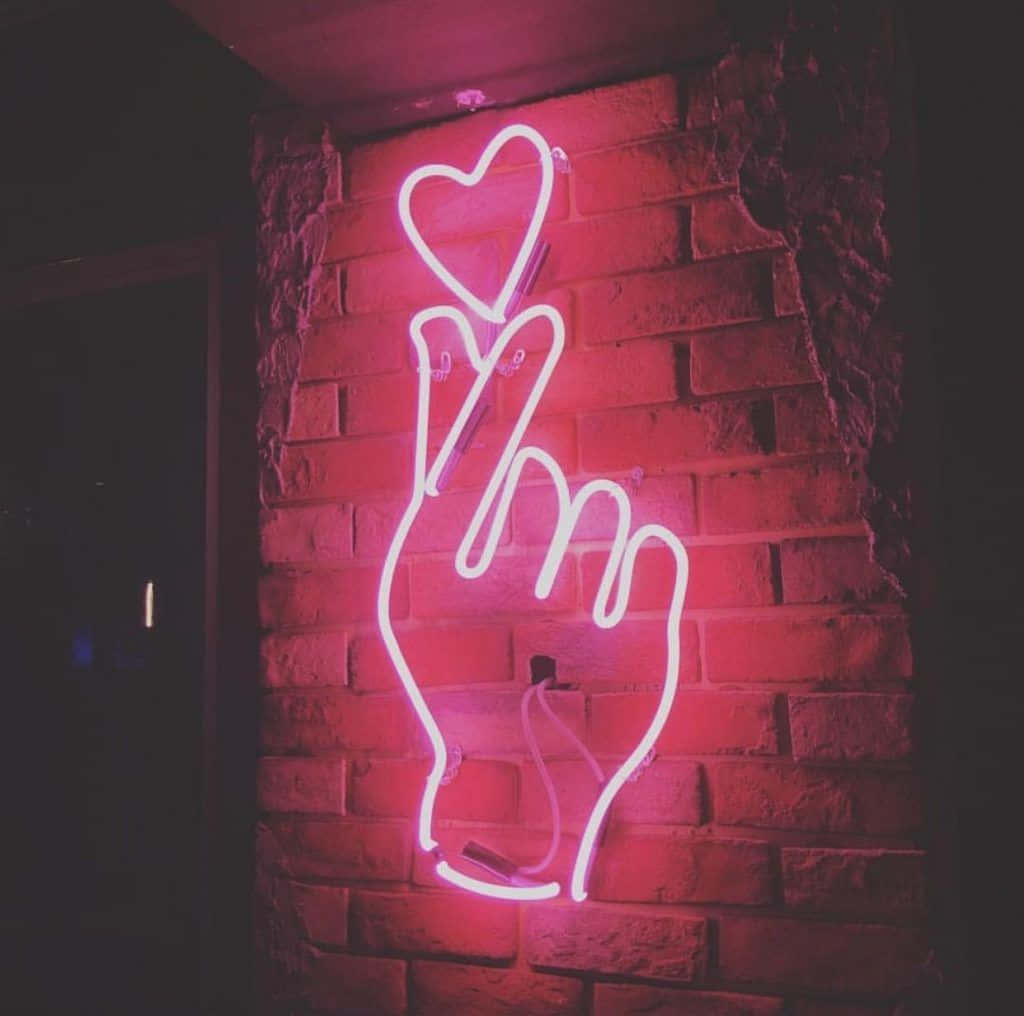 A Pink Neon Sign With A Hand Holding A Heart Wallpaper