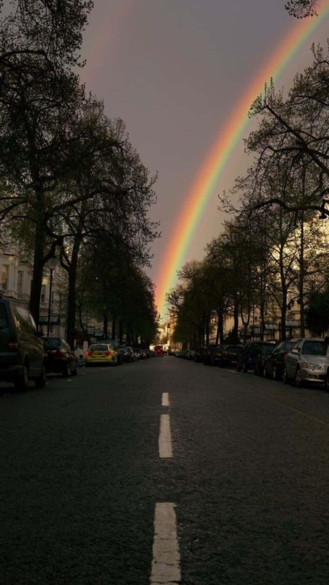 A Rainbow Is Seen Over A Street With Cars Parked In The Street Wallpaper