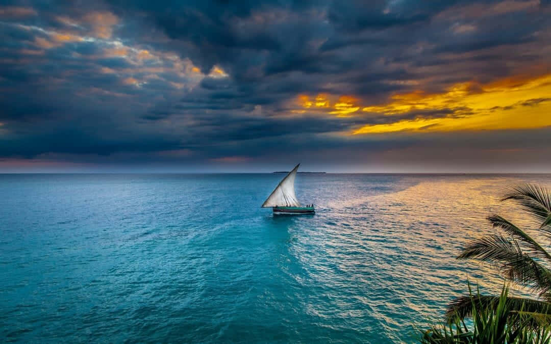 A Sailboat Sails In The Ocean At Sunset Wallpaper