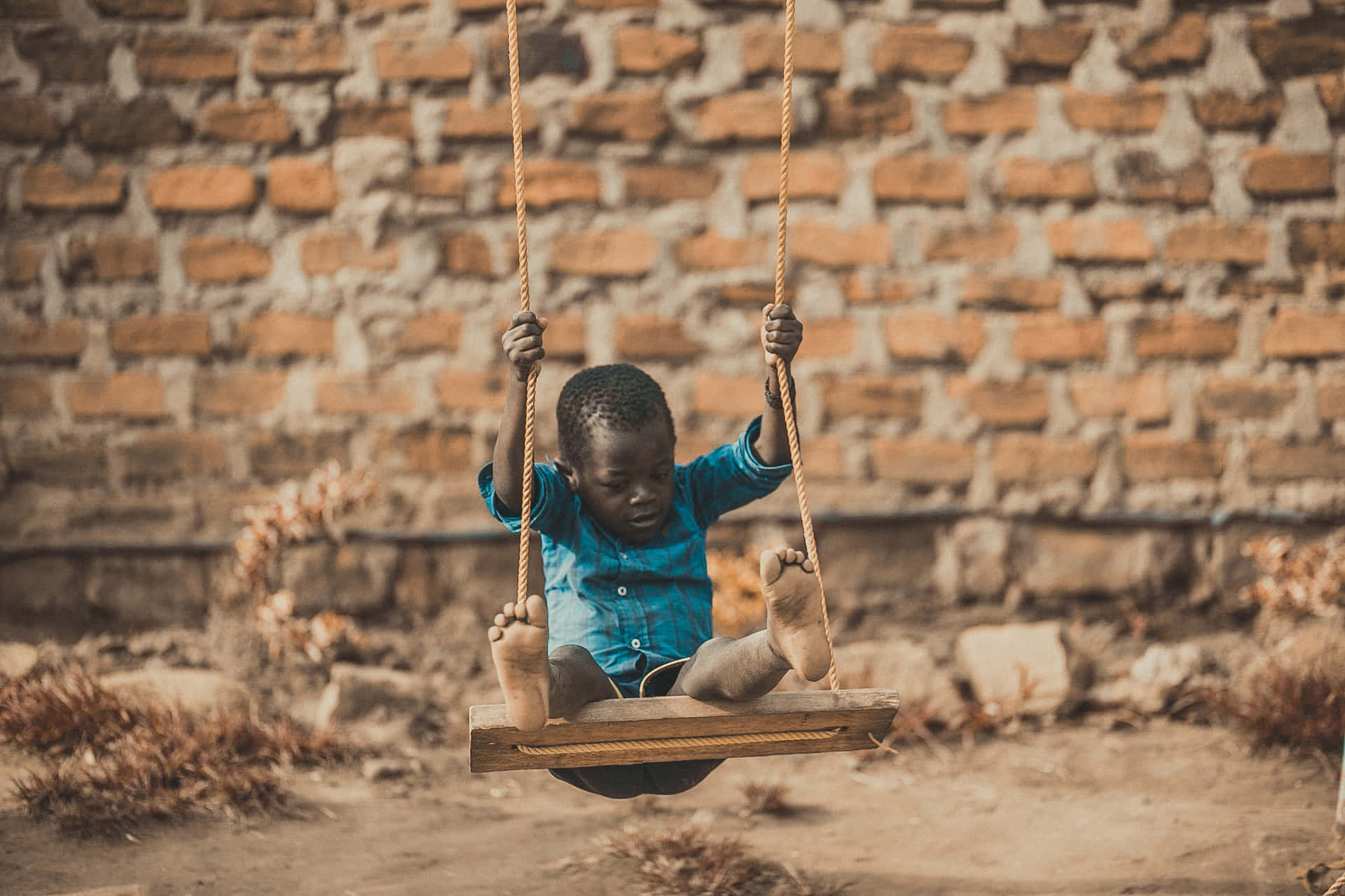 A Child Is Swinging On A Swing In Front Of A Brick Wall Wallpaper
