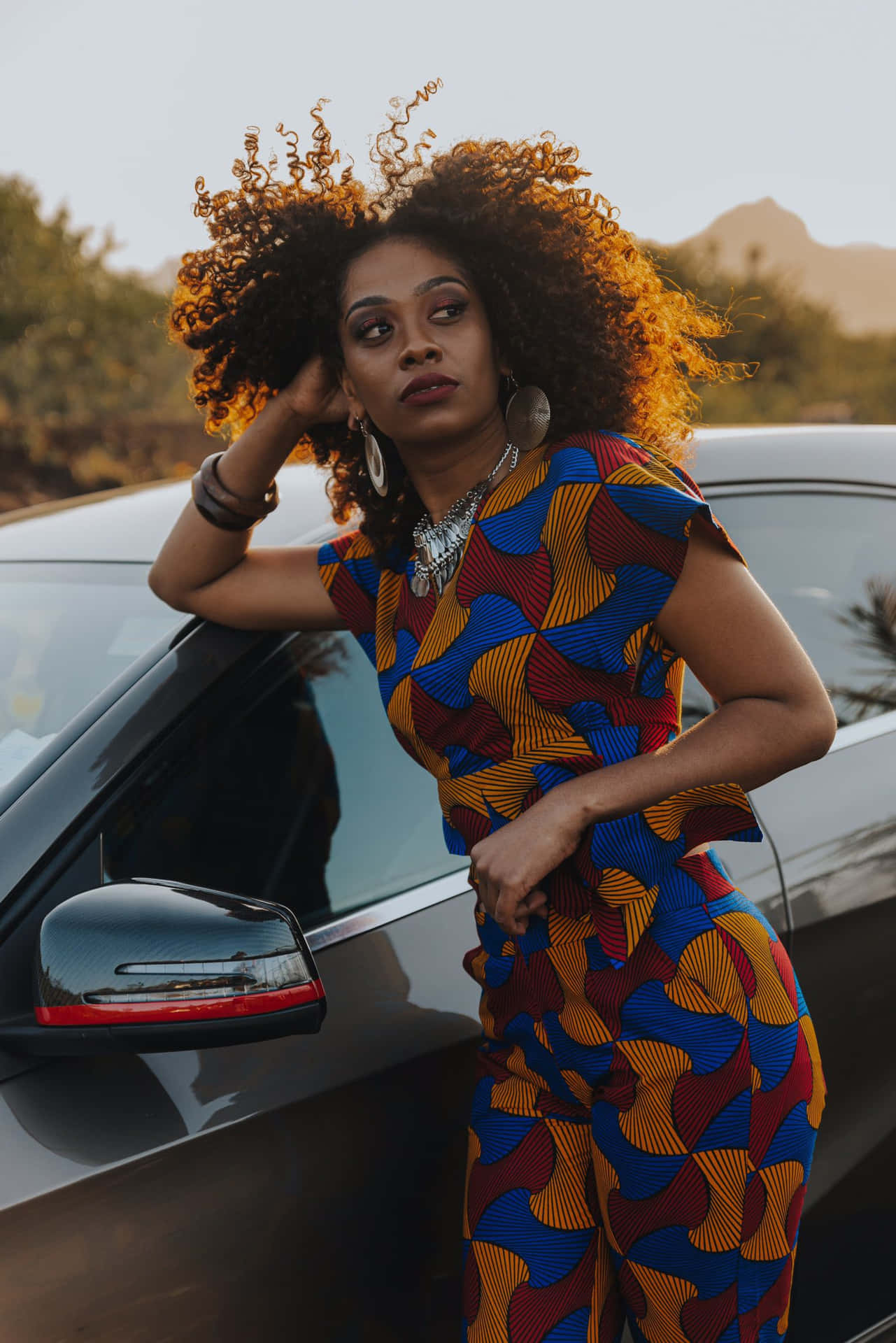 A Woman In A Colorful Jumpsuit Leaning Against A Car