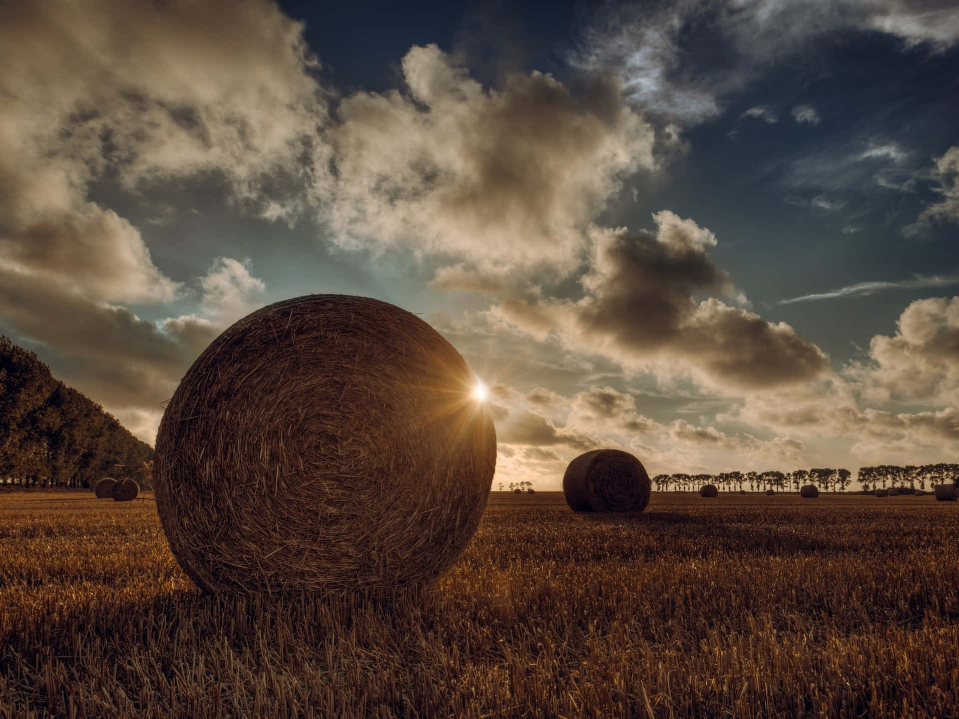 Hay Bales In A Field With The Sun Setting Behind Them