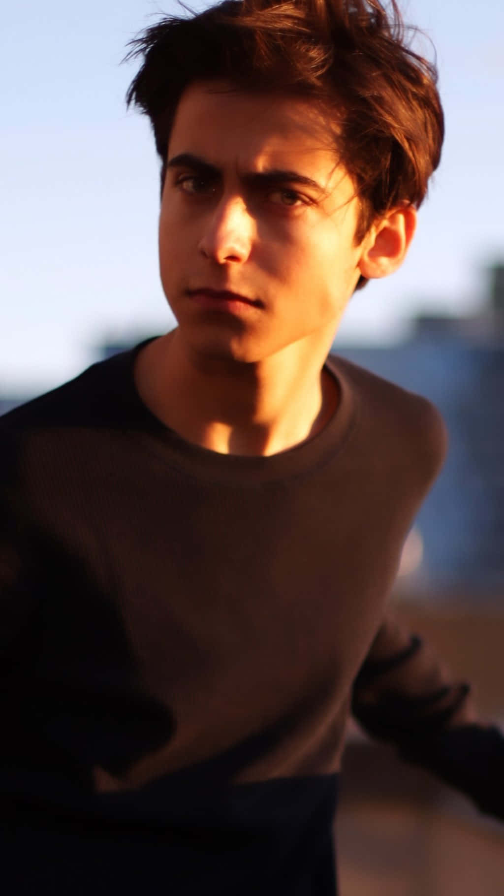 A Young Man In A Black Shirt Is Looking At The Camera Wallpaper