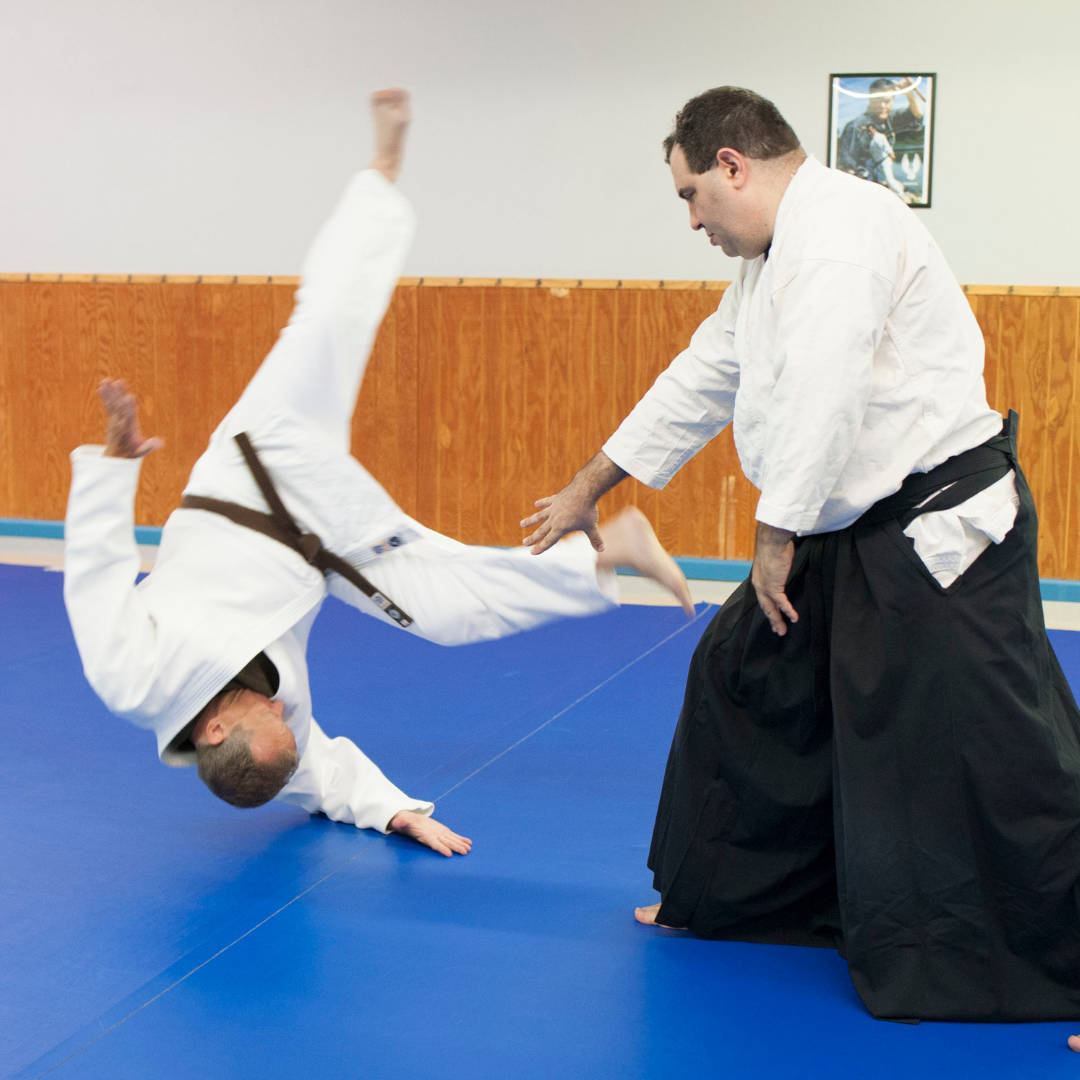 An Aikido practitioner executing a dynamic Aiki-Nage technique in a Dojo Wallpaper