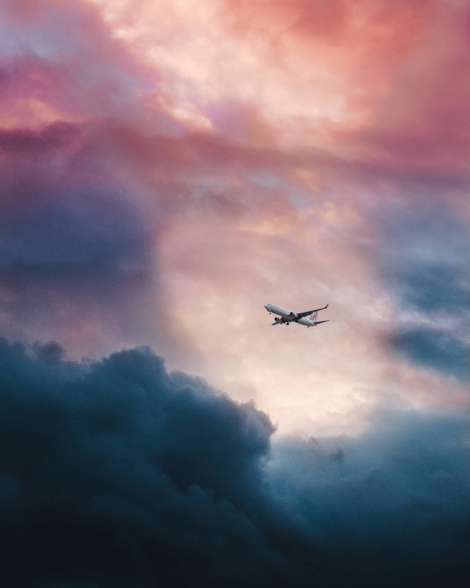 Aerial view of airplane flying above pink and blue clouds. Wallpaper