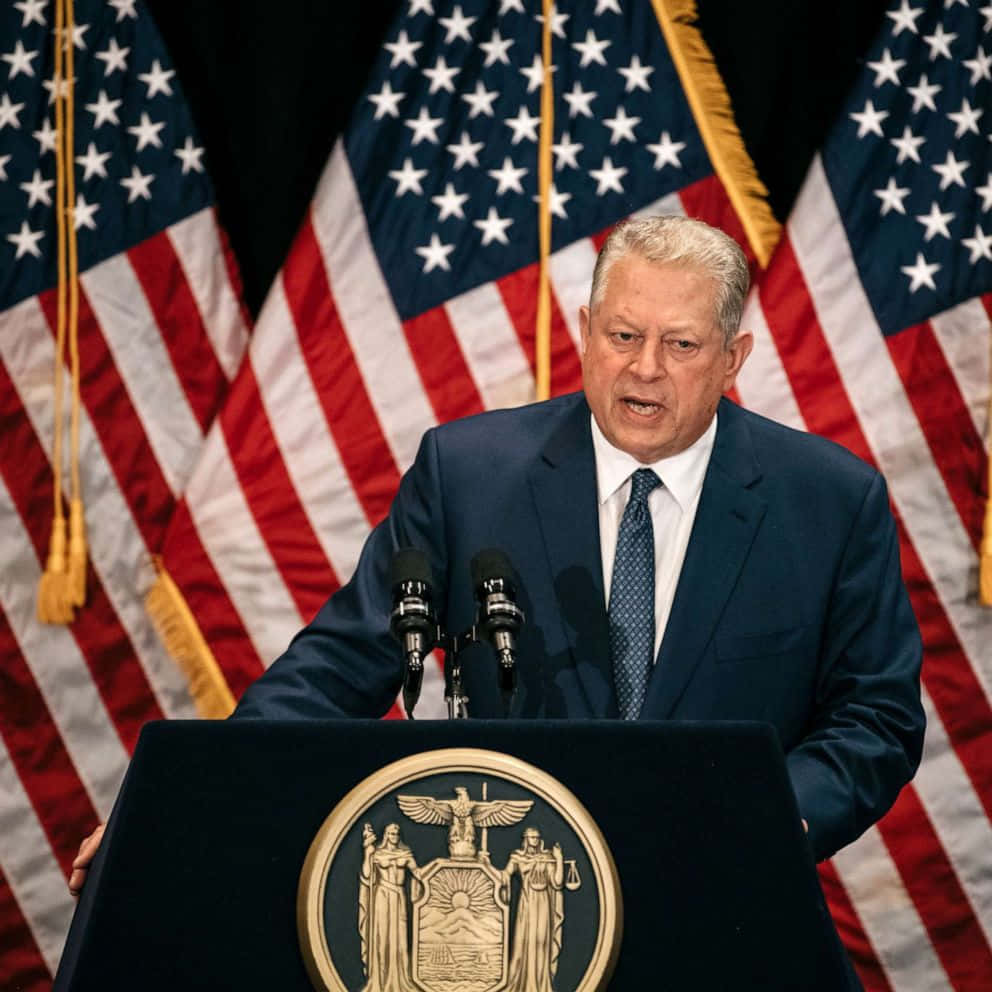 Al Gore Speaking On A Podium With Three American Flags Wallpaper