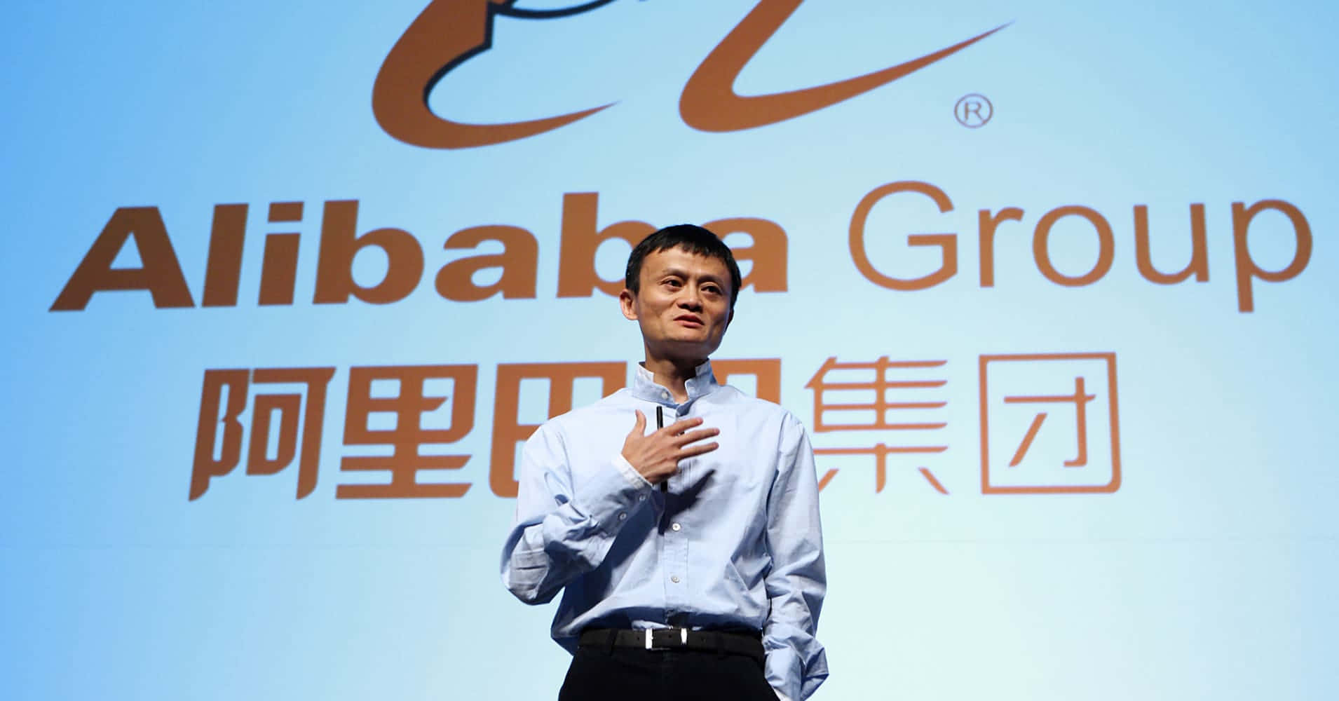 A Man Standing In Front Of A Logo For Alibaba Group