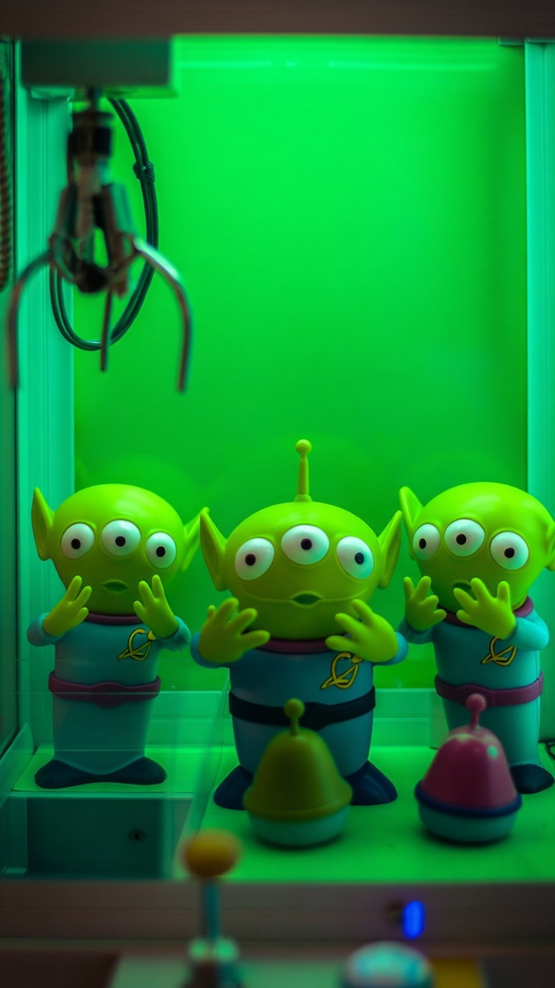 Alien Worship Claw Wallpaper — Three green three-eyed alien toys in a claw machine bathed in neon green light.