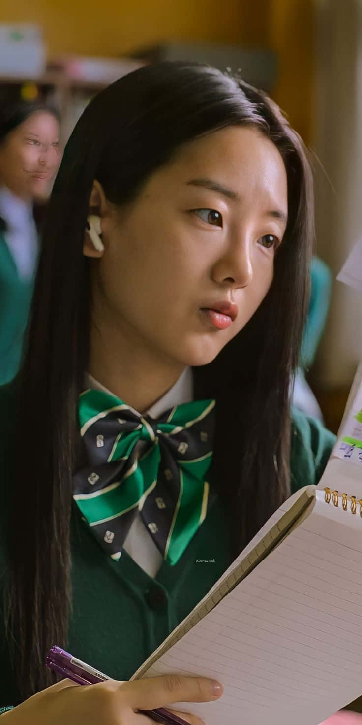 A Girl In Green Uniform Is Holding A Notebook