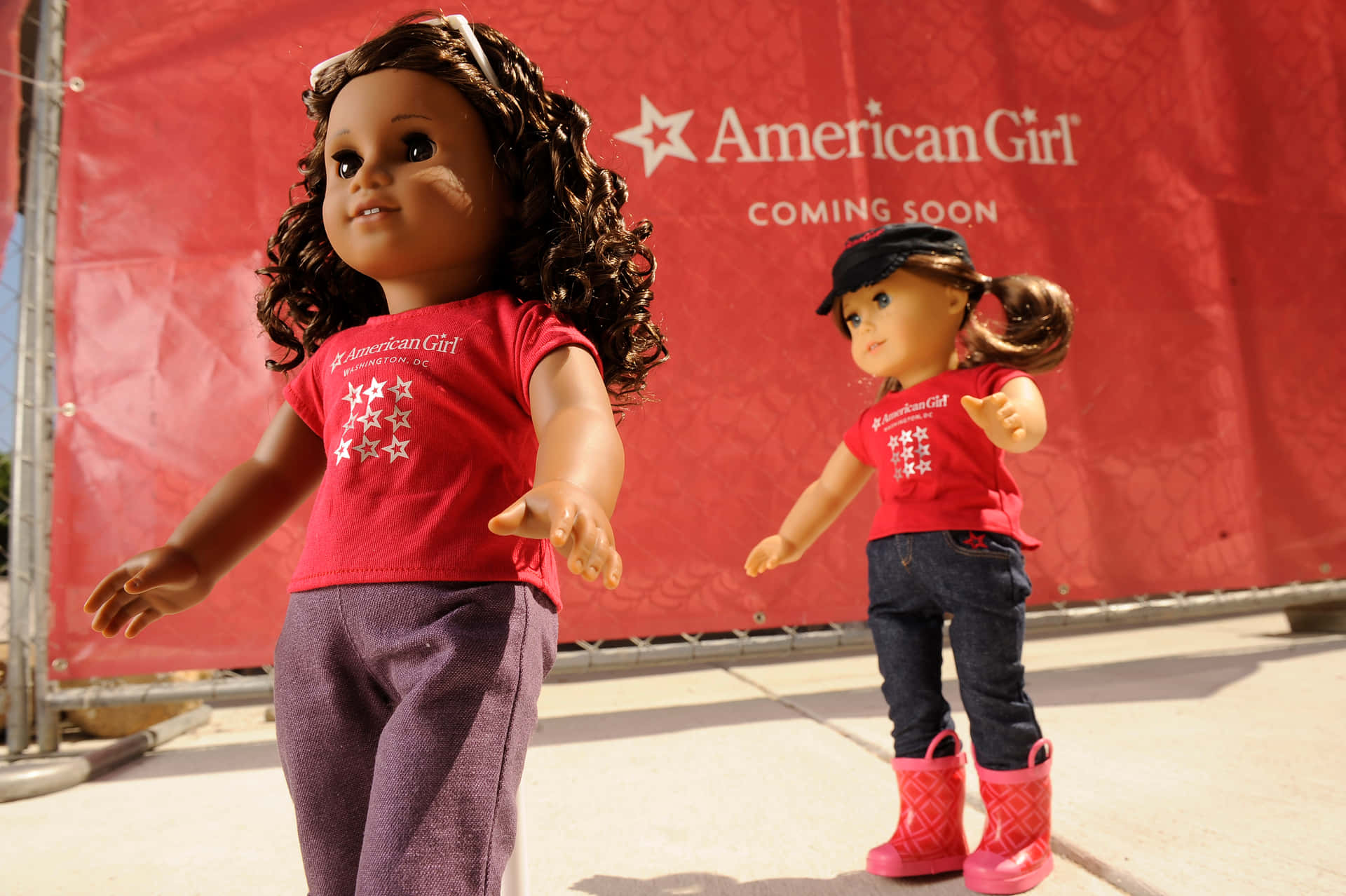 Two American Girl Dolls Standing Next To A Red Fence