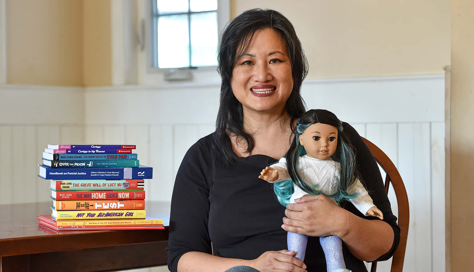 A Woman Sitting At A Table With A Doll And Books