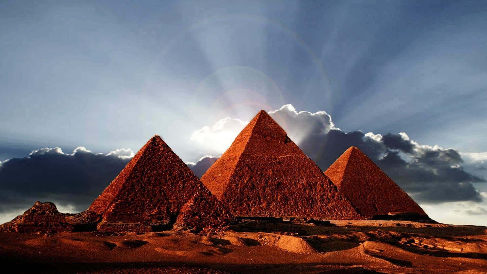 Three Pyramids In The Desert With Sun Shining On Them Wallpaper