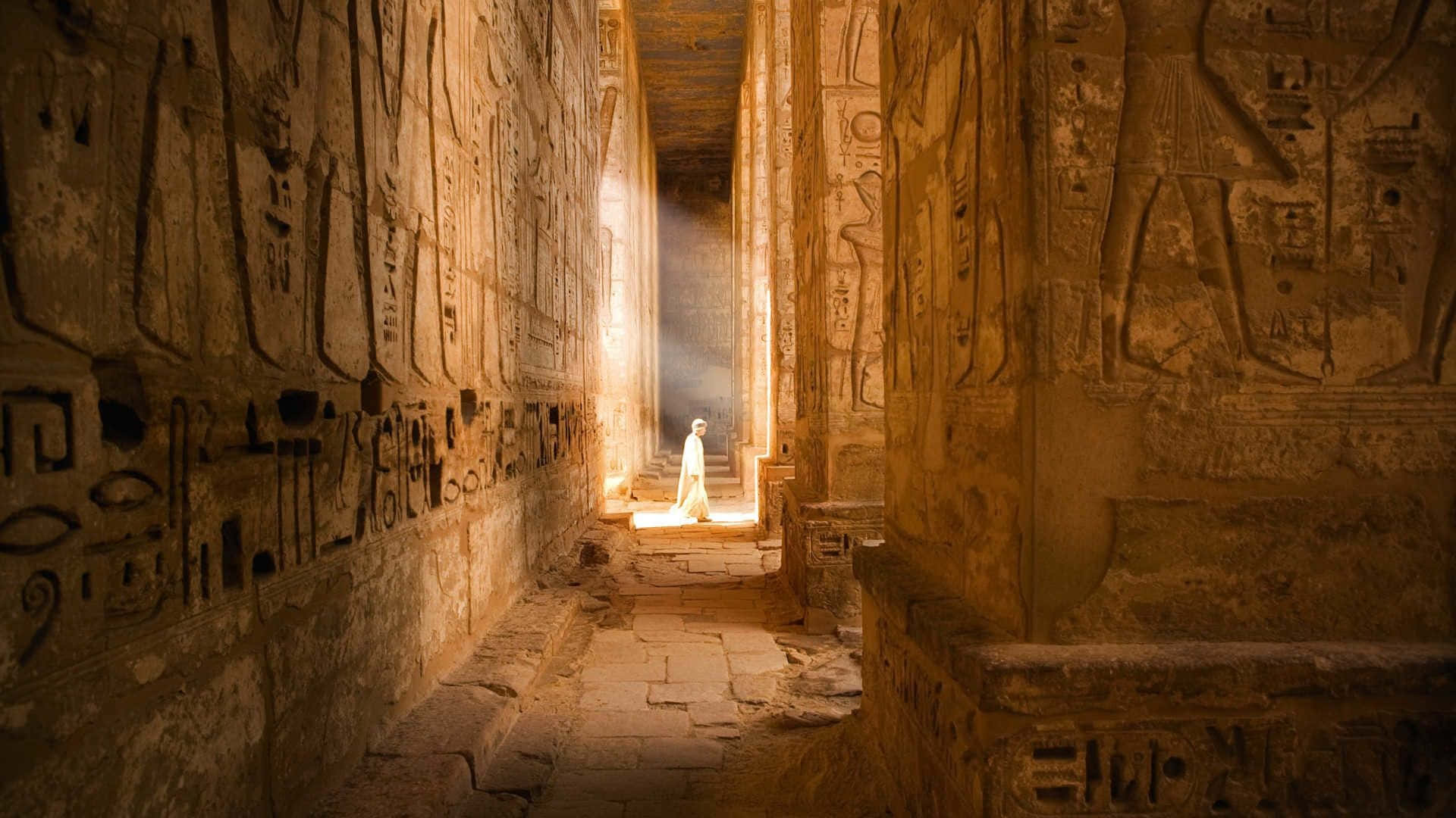 A Man Is Walking Down A Narrow Hallway In An Ancient Egyptian Temple Wallpaper