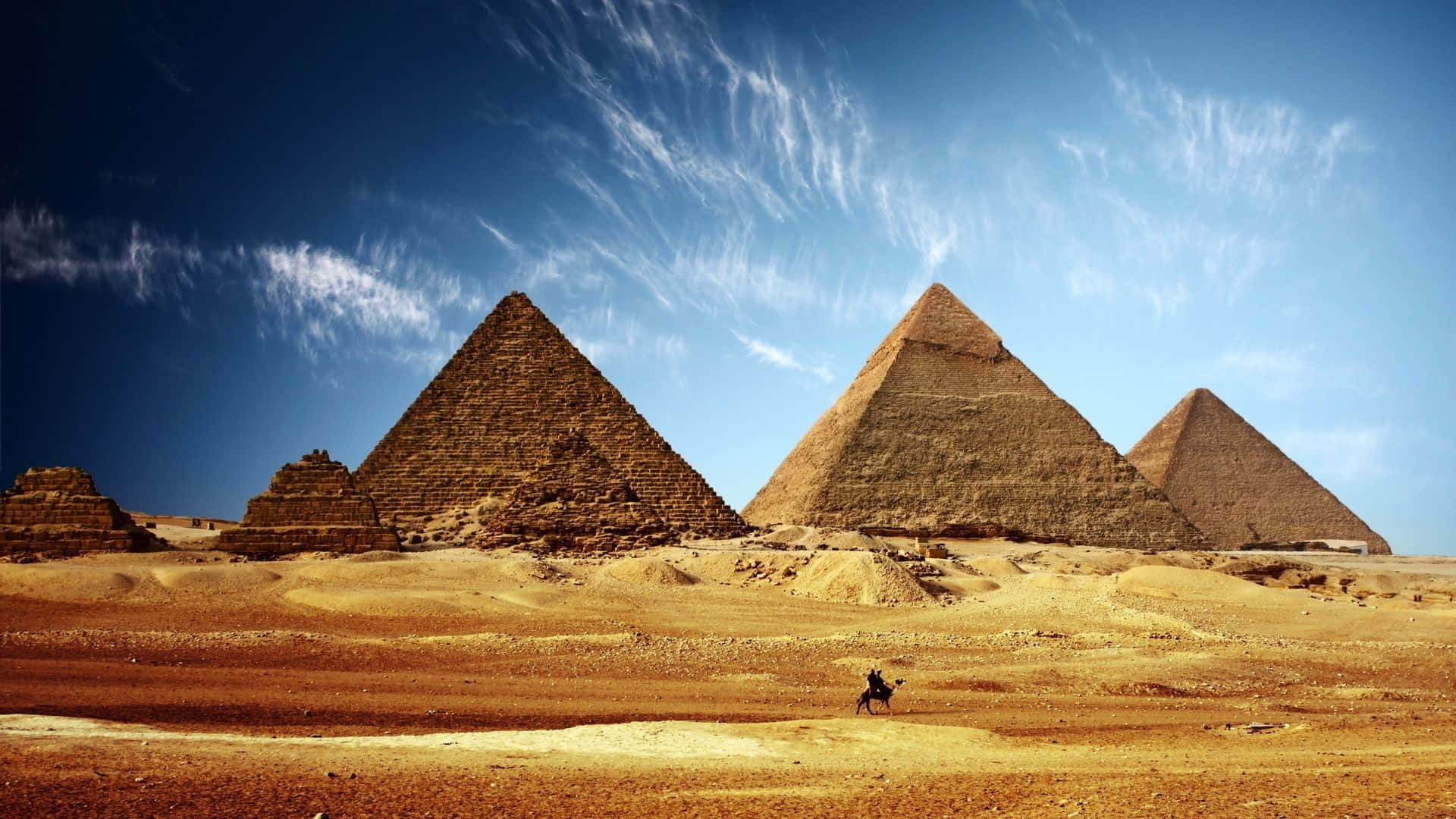A Man Walks Through The Desert With The Pyramids In The Background Wallpaper